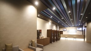 Un hall d’hôtel moderne avec un comptoir d’accueil, un espace salon et un écran de télévision.