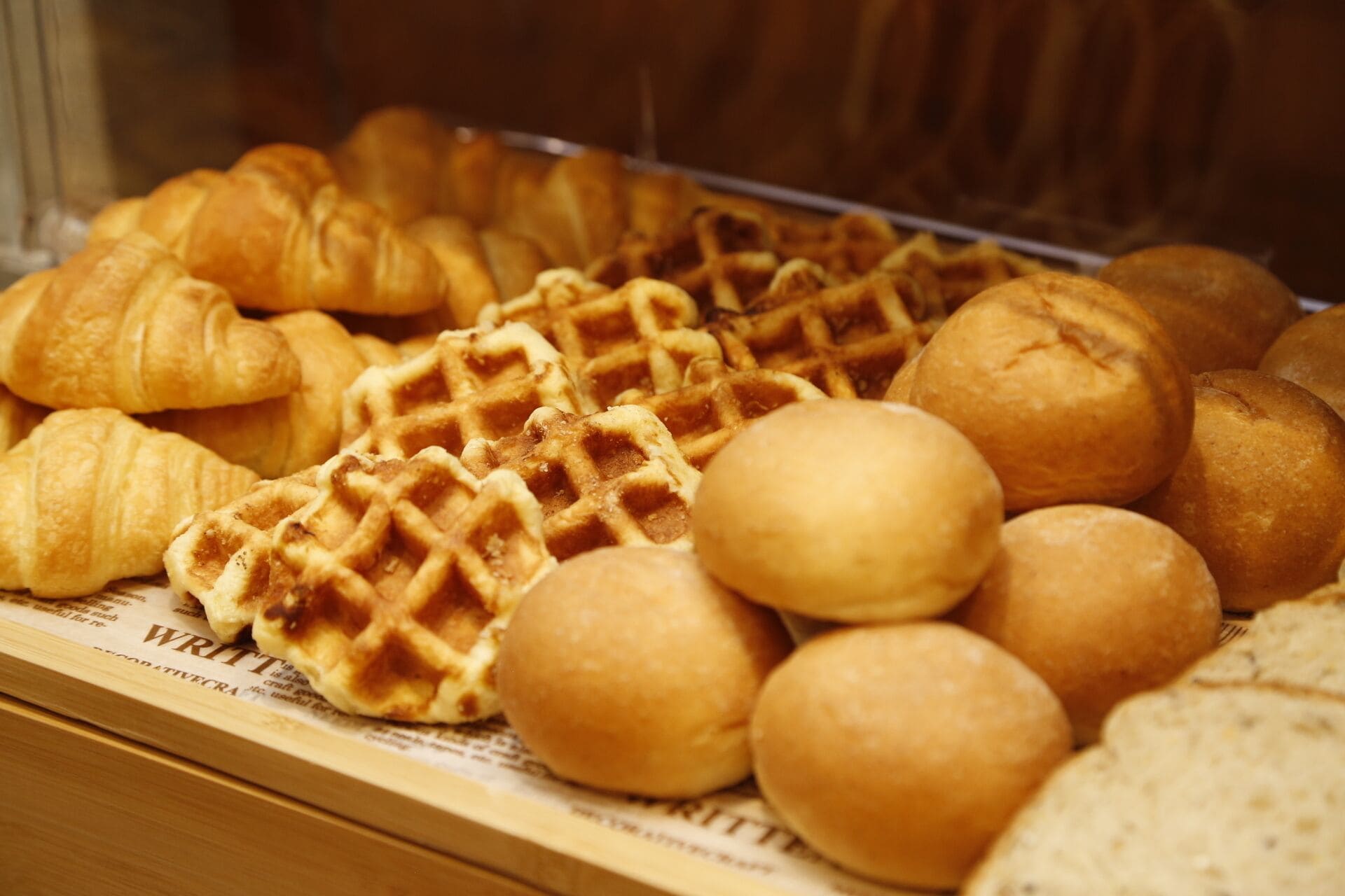 A display of various baked goods including croissants, waffles, and round bread rolls.