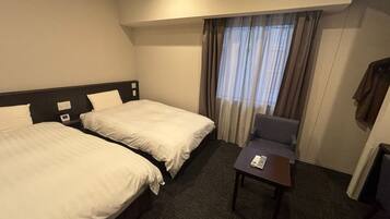 A hotel room with two beds, a small table, and a chair.