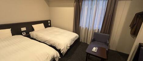 A hotel room with two beds, a small table, and a chair.