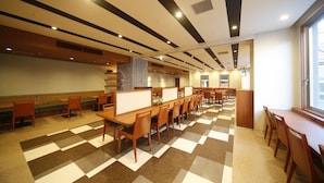 Un vaste espace dédié à la salle à manger, avec de nombreuses tables et des banquettes, un sol à motifs et une grande fenêtre laissant entrer la lumière naturelle.