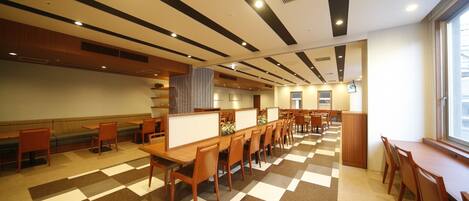 A spacious dining area with multiple tables and booths, a patterned floor, and a large window providing natural light.