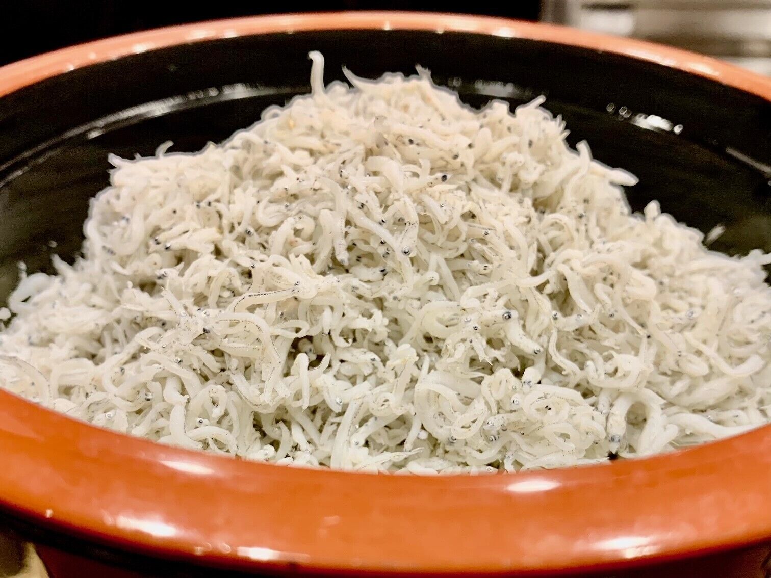 Uma tigela com material branco desfiado, possivelmente comida, em uma tigela preta e laranja.