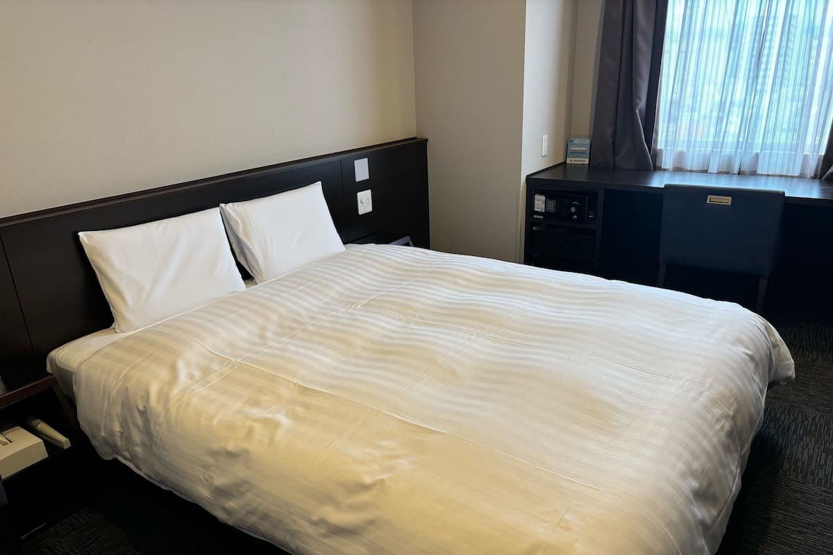 A hotel room with a bed, a desk, and a window with curtains.