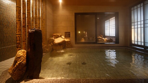 Une piscine intérieure de style japonais traditionnel, agrémentée d’éléments en pierre et dotée d’une grande porte-fenêtre coulissante.