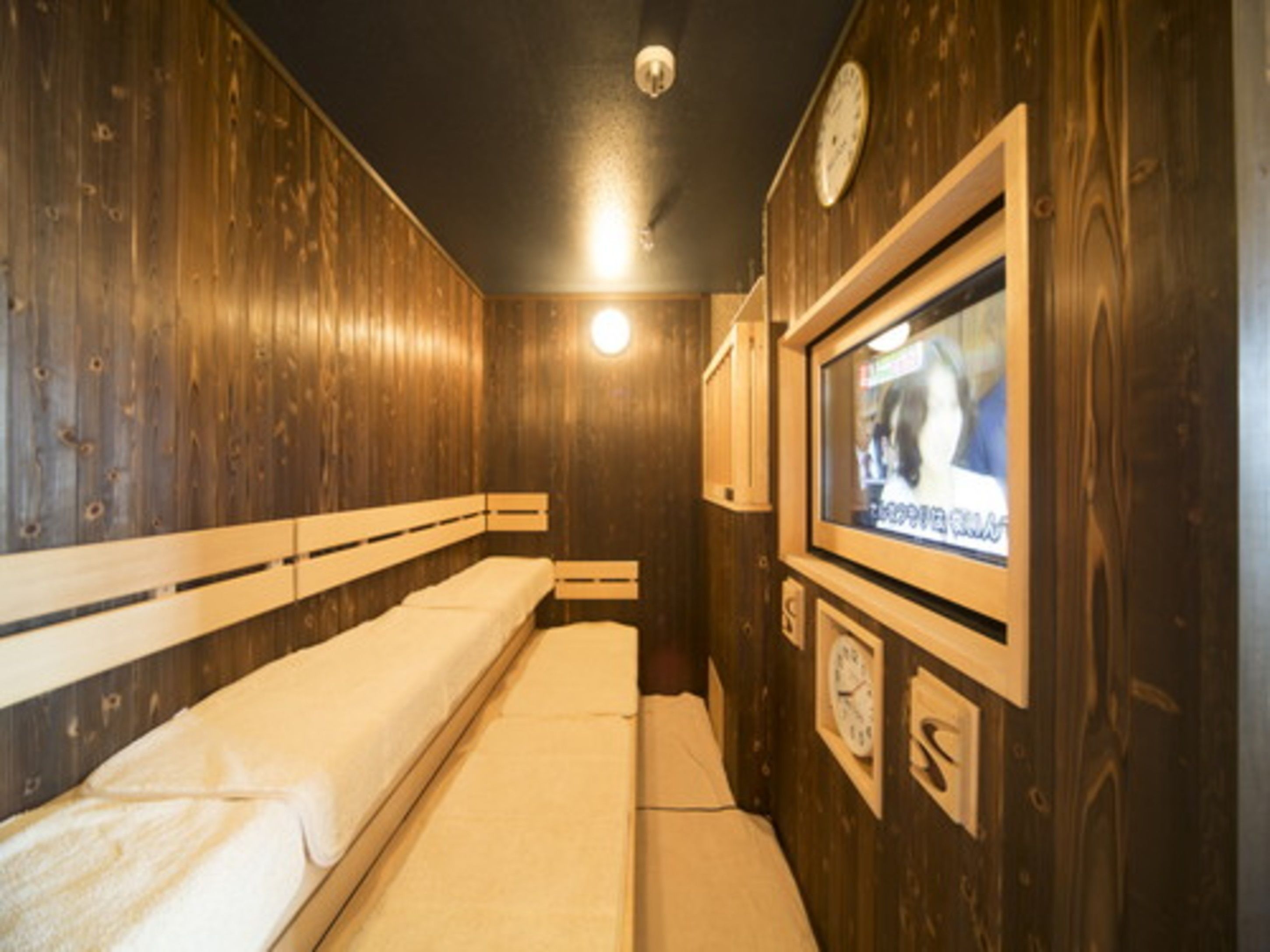 A small, cozy room with wooden walls, a single bed, a television, and a clock.