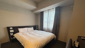 Une chambre d’hôtel avec un grand lit, une table de chevet avec une lampe et une fenêtre avec des rideaux.