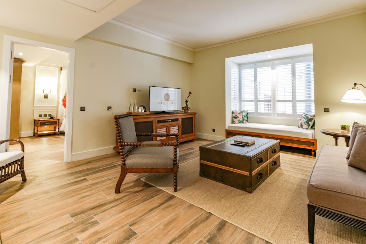 A living room with a wooden floor, a sofa, a coffee table, a TV, and a window with blinds.