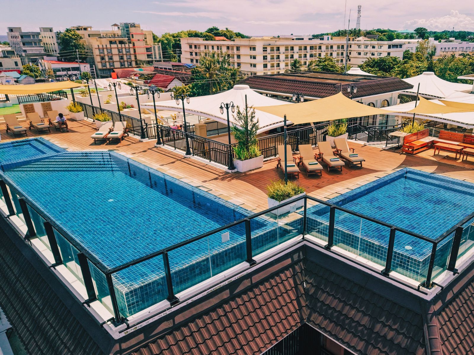 A rooftop swimming pool with multiple sections, sun loungers, and umbrellas.