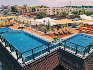 Una piscina en la azotea con varias secciones, tumbonas y sombrillas.