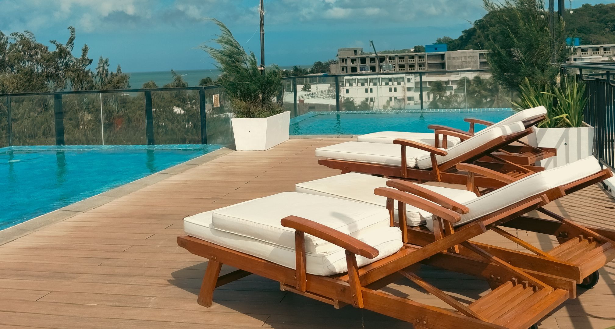 Zona junto a la piscina con sillones de madera y vista al océano.