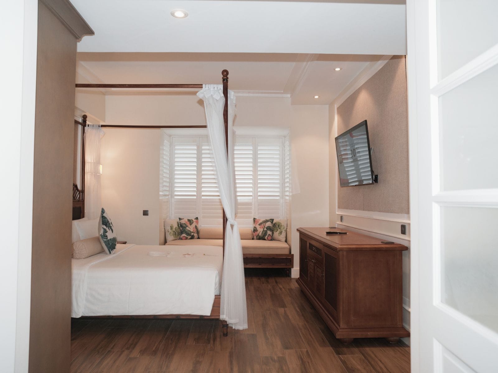 A bedroom with a four-poster bed, a wooden cabinet, and a television mounted on the wall.
