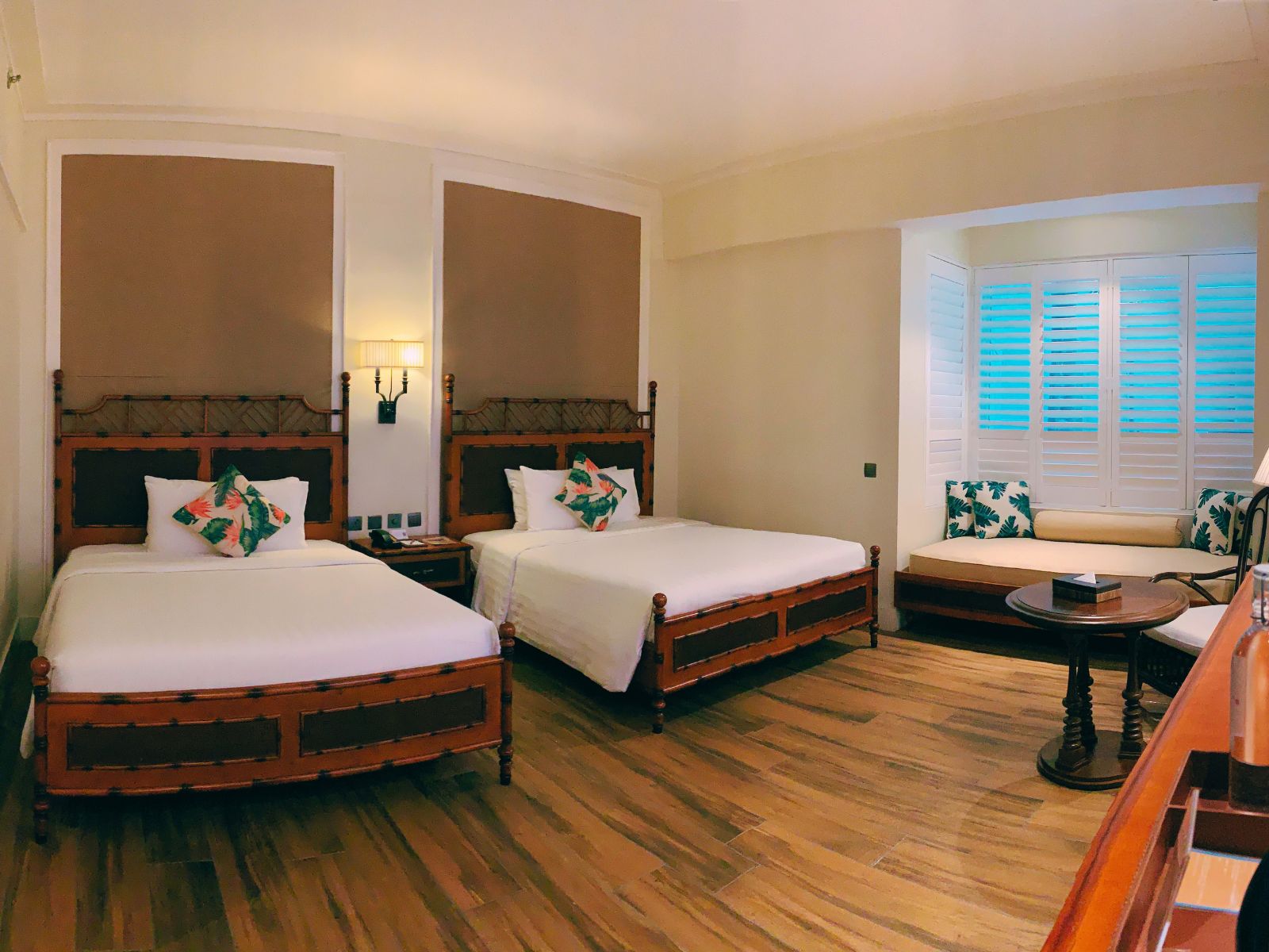A hotel room with two beds, a sofa, a small table, and a window with shutters.