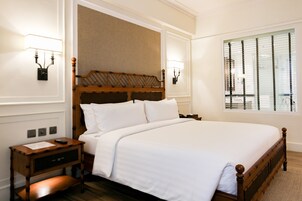 A neatly made bed with a wooden headboard, a bedside table with a lamp, and a window with blinds.