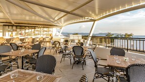 Un espace de restauration en plein air avec des chaises et des tables en osier, un bar avec des bouteilles exposées et une vue sur la mer.