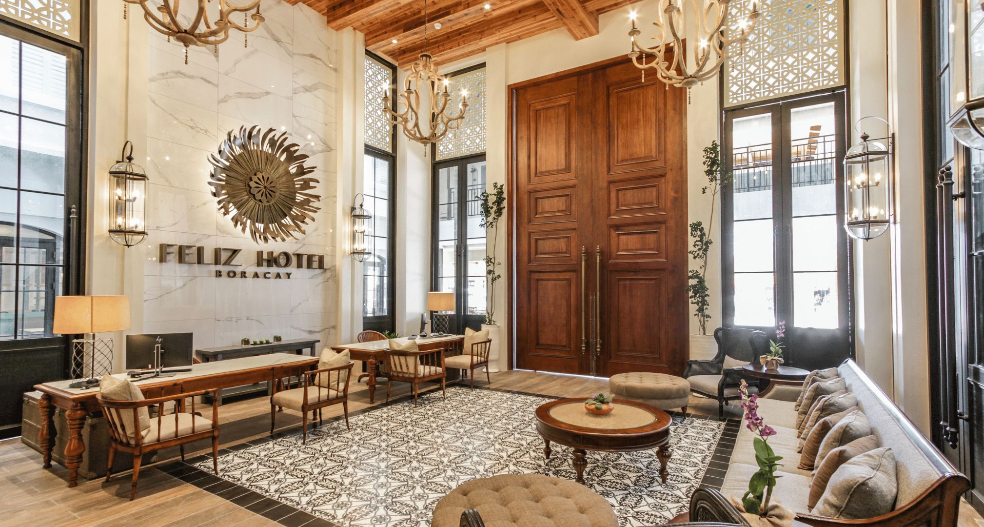 Eine Hotelhalle mit einer großen Holztür, einem Chandelier, einer Wanduhr und einer Sitzecke mit einem gemusterten Teppich.