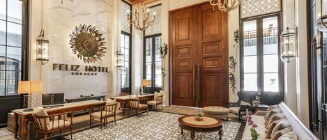 Eine Hotelhalle mit einer großen Holztür, einem Chandelier, einer Wanduhr und einer Sitzecke mit einem gemusterten Teppich.