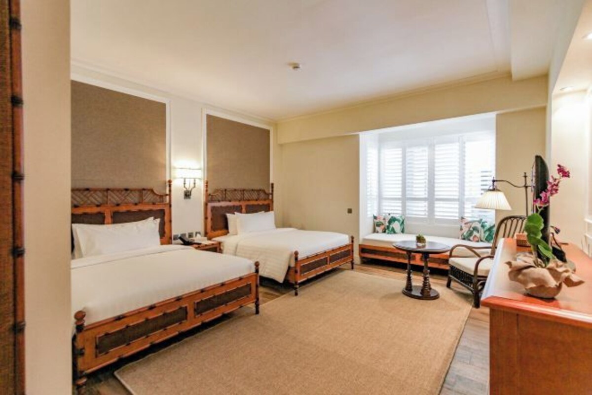 Une chambre d’hôtel avec deux lits en bois, une petite table, une chaise et un bureau avec une lampe.