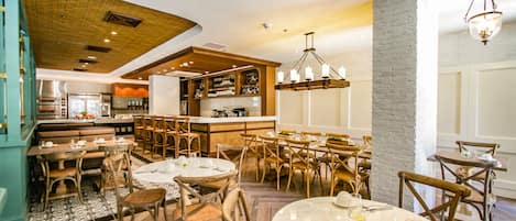 A restaurant with wooden furniture, a bar area, and a kitchen in the background.