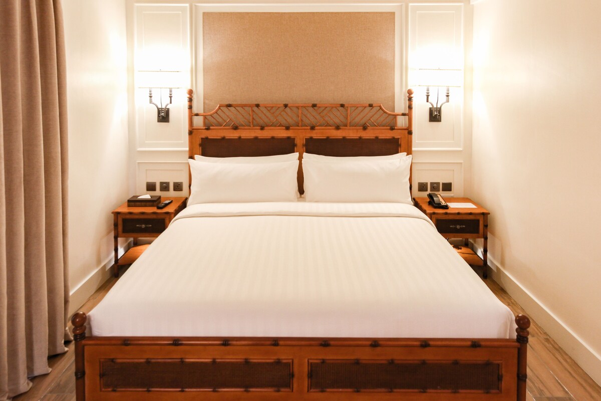 Una cama grande y bien hecha con un cabecero de madera y dos mesitas de noche, cada una con una lámpara y un teléfono.