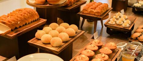 A buffet with various baked goods including bread, rolls, and muffins.