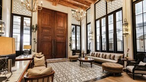 Un salon spacieux avec une grande porte en bois, un ensemble de canapés, une table basse et un tapis à motifs.