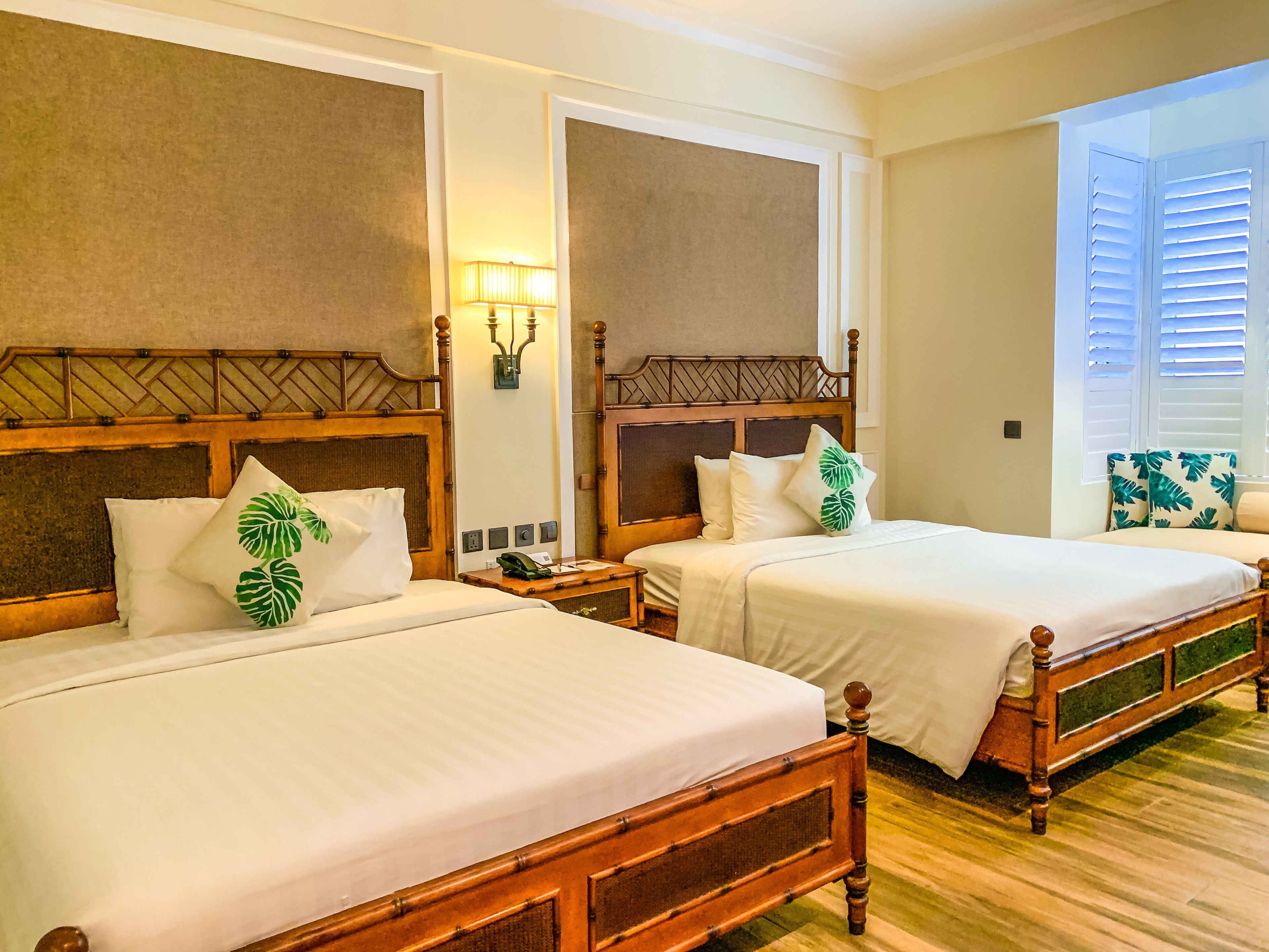 Quarto de hotel com duas camas, cabeceiras de madeira e mesa de cabeceira com abajur.
