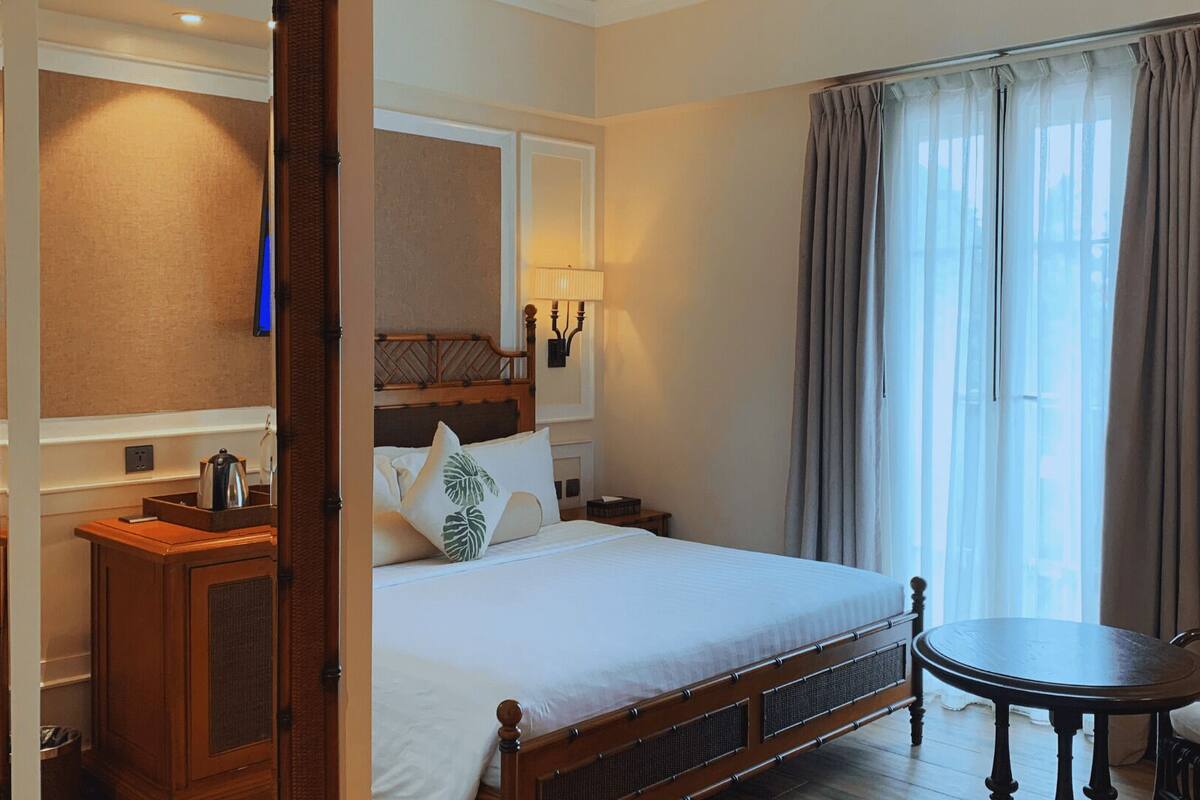 A hotel room with a bed, bedside table, lamp, and a chair.