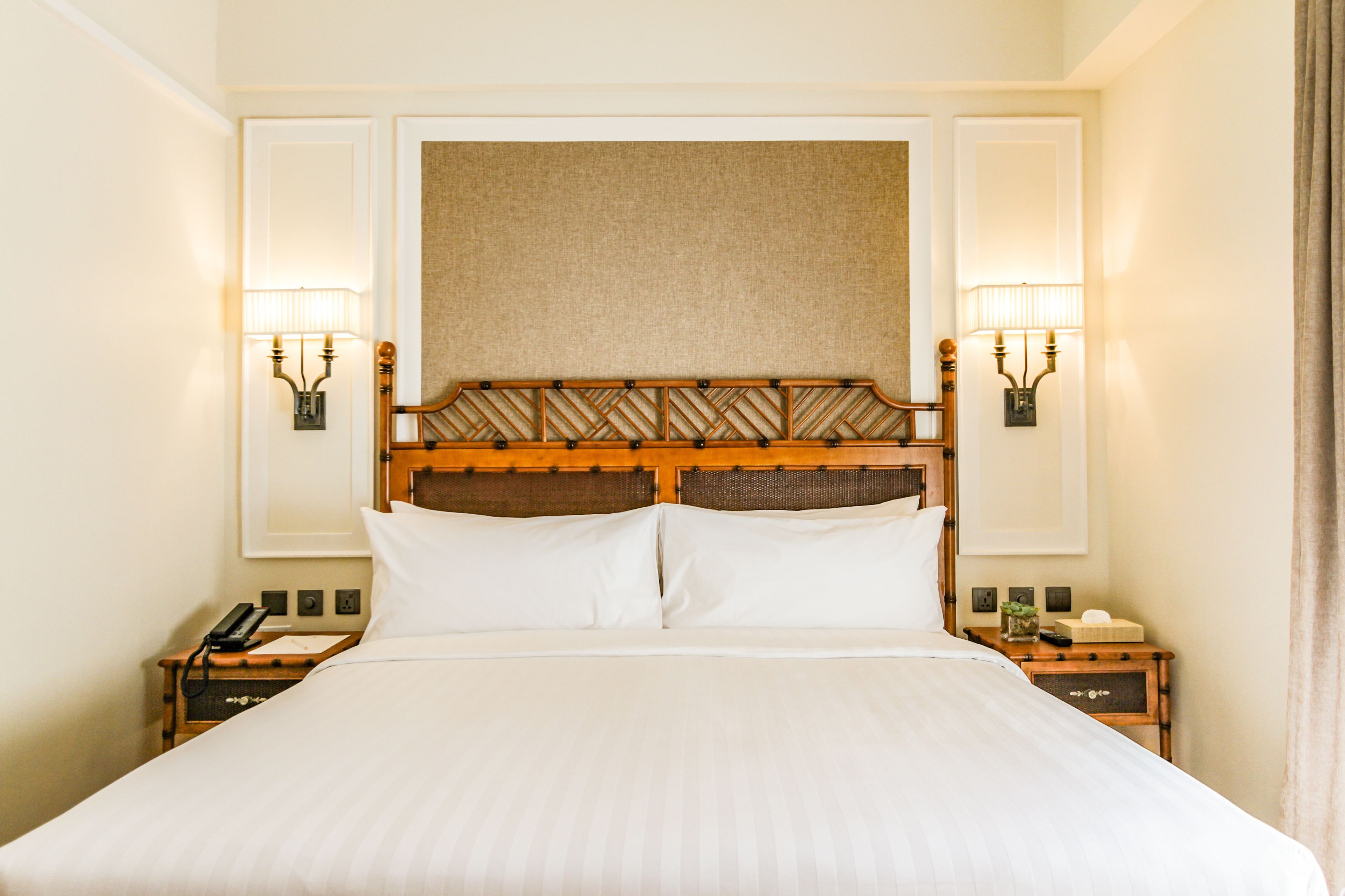 A hotel room with a large bed, two bedside tables, a wooden headboard, and wall-mounted lamps.