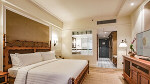 Une chambre d’hôtel avec un grand lit, une tête de lit en bois, une télévision, un bureau et une salle de bain visible à travers une porte ouverte.