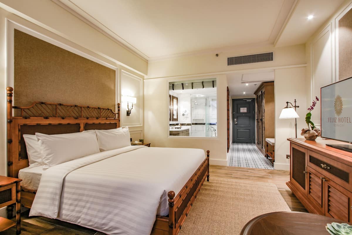 A hotel room with a large bed, a wooden headboard, a television, a desk, and a bathroom visible through an open door.