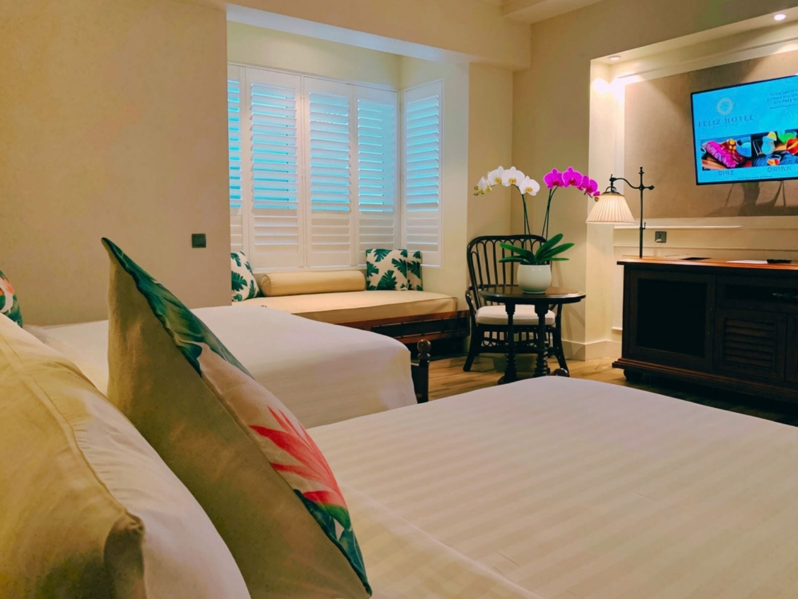 Habitación de hotel con dos camas, zona de estar, televisor y ventana con persianas.