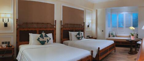 A hotel room with two wooden beds, a small table, and a window with shutters.