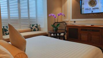 A hotel room with a bed, a seating area with a view of the window, a television on the wall, and a potted plant.