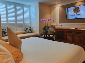Habitación de hotel con cama, zona de estar con vista a la ventana, televisor en la pared y planta en maceta.