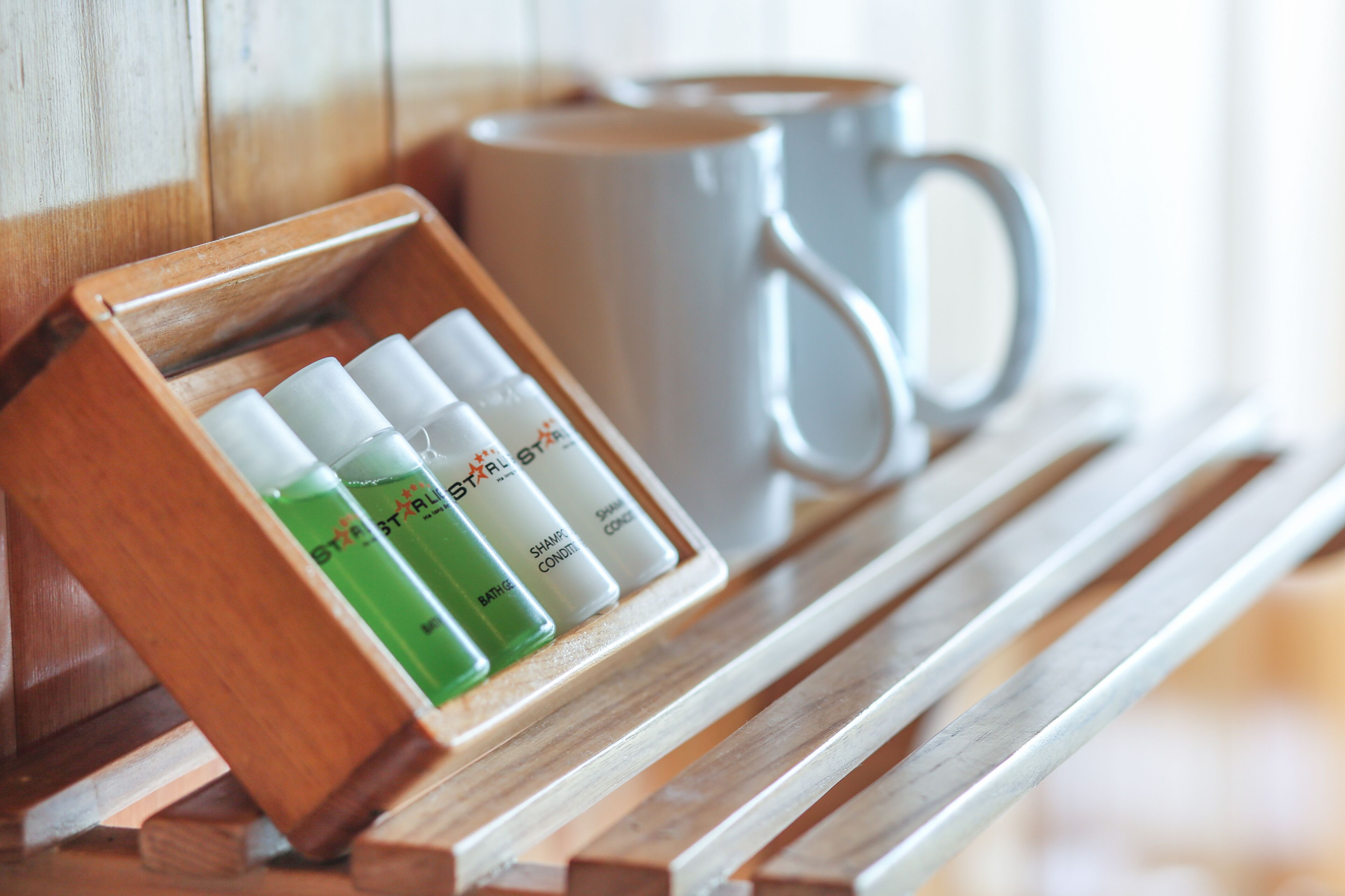 A wooden tray with three bottles of shampoo and conditioner, a white mug, and a wooden bench.