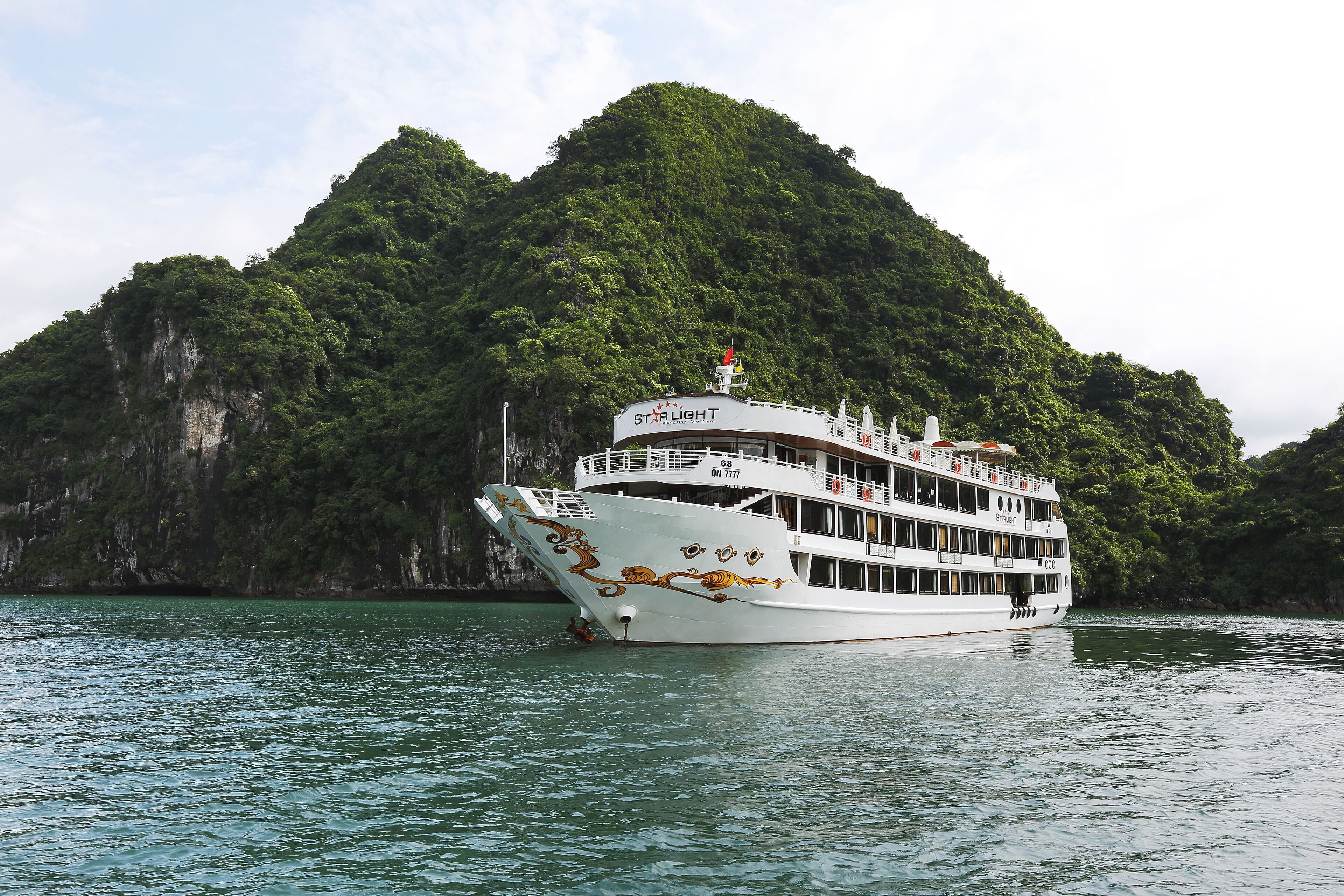 A large white river cruise ship with multiple decks and a dragon design on its side, sailing near a lush green mountain.