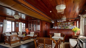 A traditional wooden interior with a bar area, seating arrangements, and a view of the city. - Garden Bay Legend Cruise (Tuan Chau)