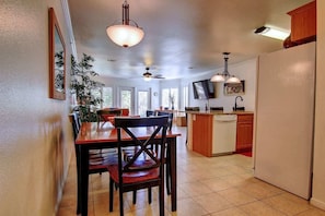 A kitchen with a dining table, chairs, a ceiling fan, and a TV mounted on the wall.