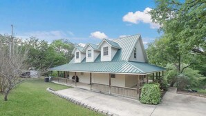A two-story house with a green metal roof, a covered porch, and a well-maintained lawn.