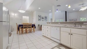 A modern kitchen with white cabinets, a dining table with chairs, and recessed ceiling lighting.