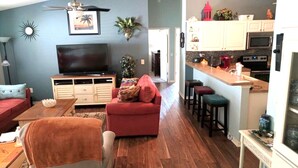 Una sala de estar con televisor, sofá rojo y una pequeña zona de comedor con taburetes.