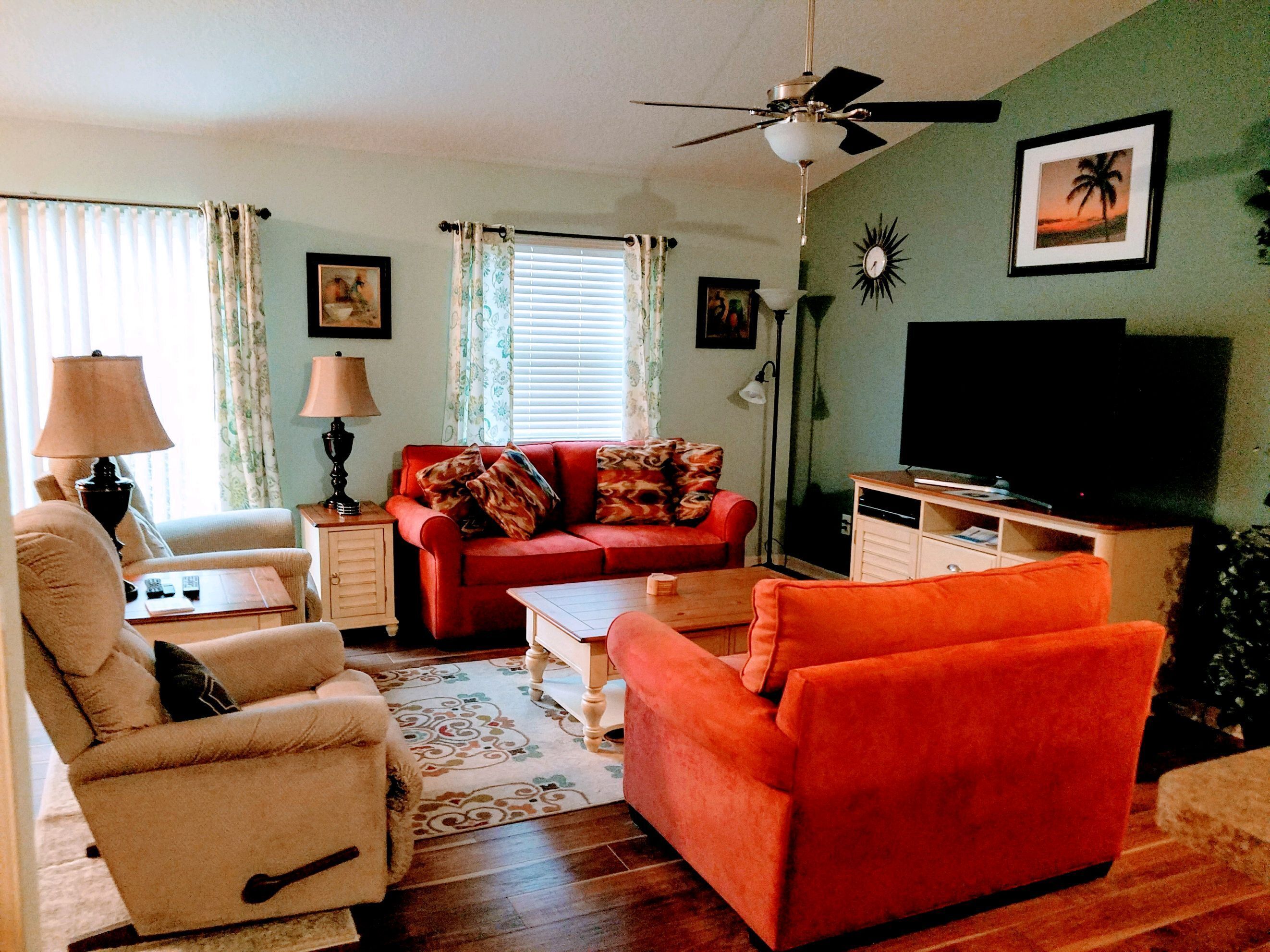 A living room with a red sofa, a white armchair, a wooden coffee table, and a television on a stand.