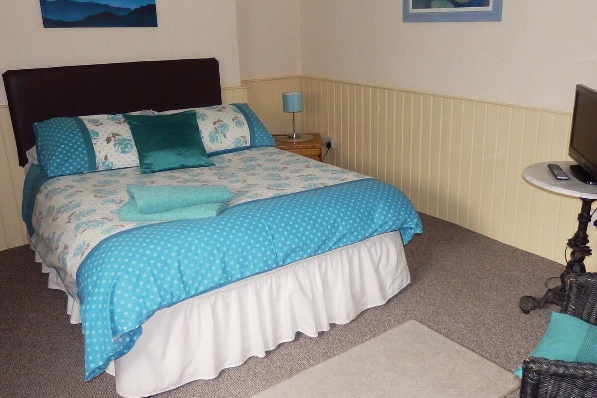 Een netjes opgemaakt bed met een blauwe stippenbeddengoed en passende kussens, een bedlamp en een klein tafeltje met een afstandsbediening.