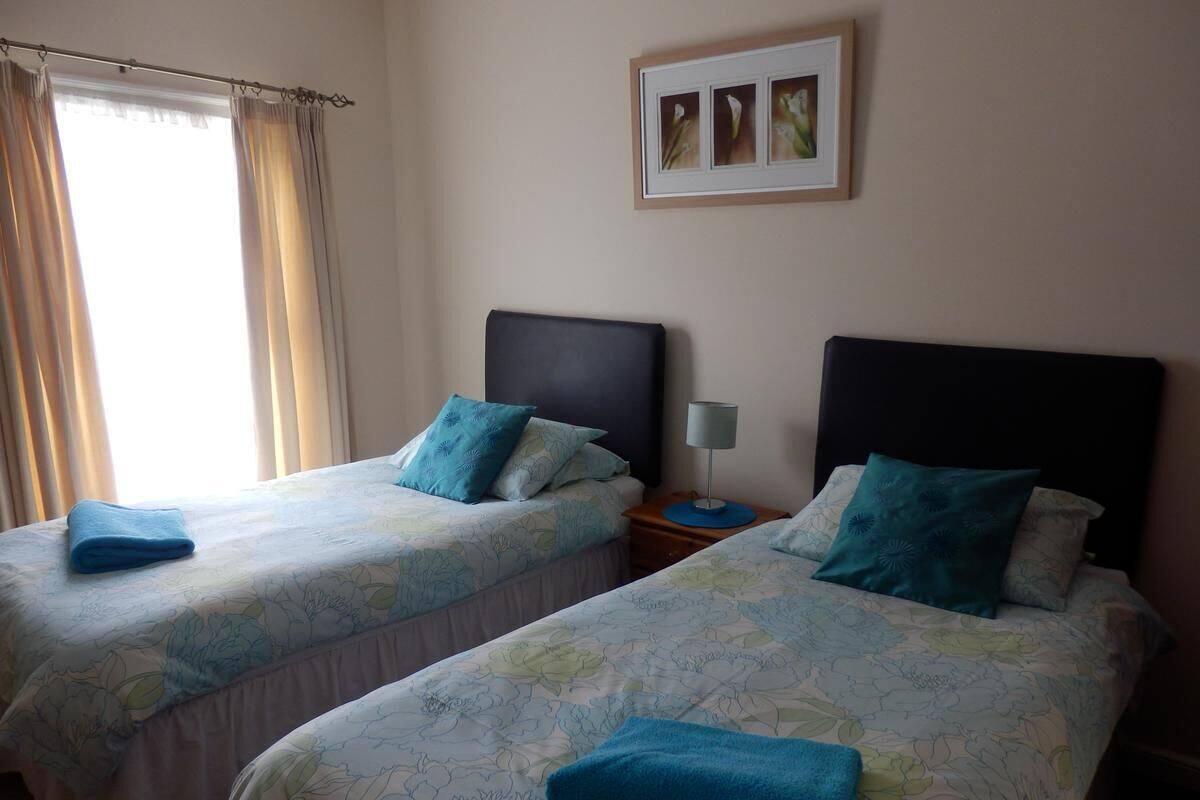 Een kamer met twee bedden, elk met hoofdeinde, nachtkastje en een ingelijst beeld aan de muur.