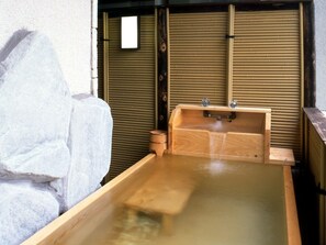 Een houten badkuip met een houten bankje, een klein houten krukje en een handdoekrek aan de muur.