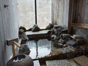 Un baño tradicional de aguas termales de piedra con escalones de madera y un balde de madera.