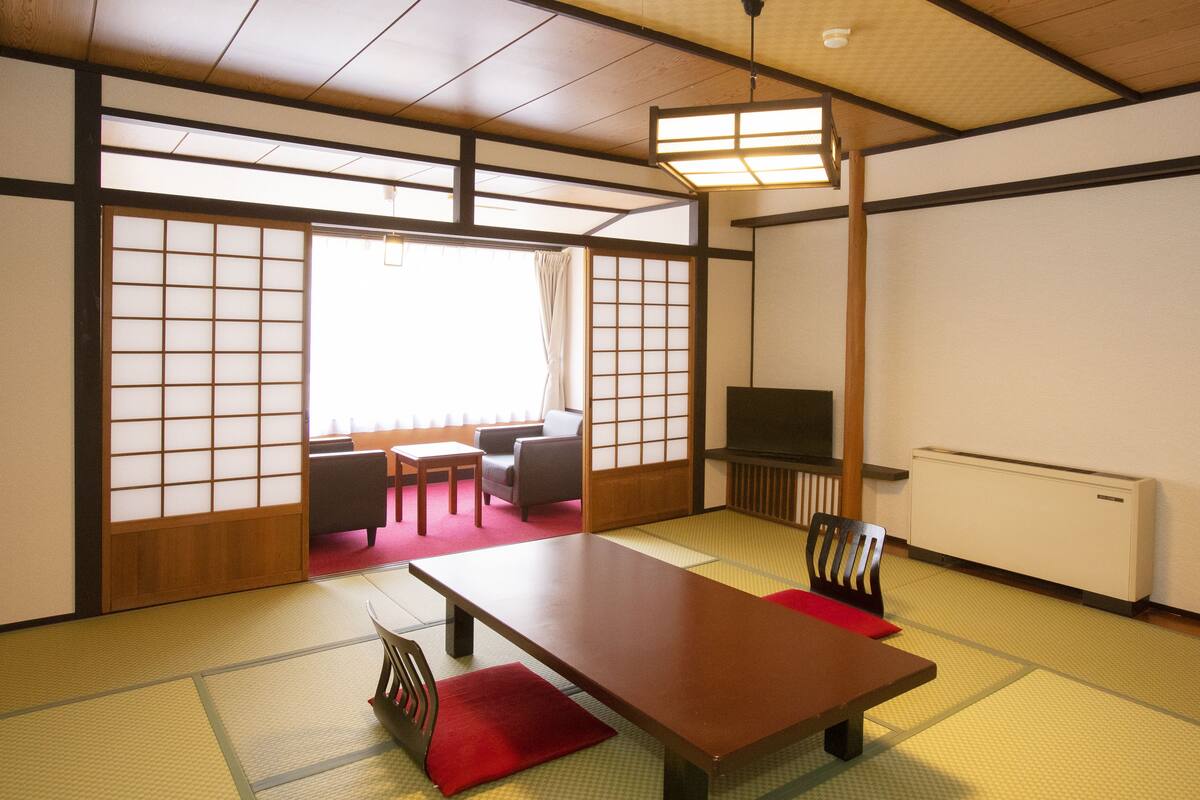 Une pièce de style japonais traditionnel, avec un sol recouvert de tatamis, une table basse, des chaises et des portes coulissantes.