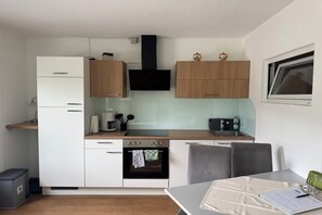 Cocina compacta con armarios blancos, extractor de aire negro y comedor con mesa y sillas.