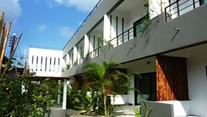 Un edificio moderno con un espacio al aire libre cubierto, un camino y vegetación.